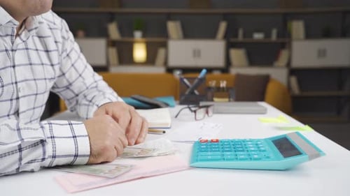 Man Counting Currency at Desk with Calculator