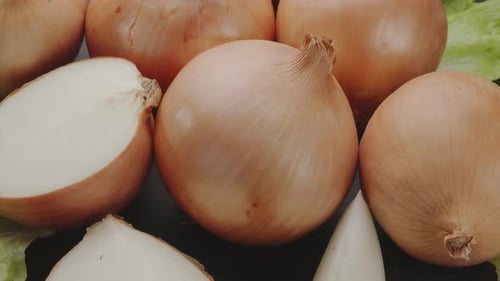 Onion bulbs with slices of onion slowly move in the frame on a gray stone table.