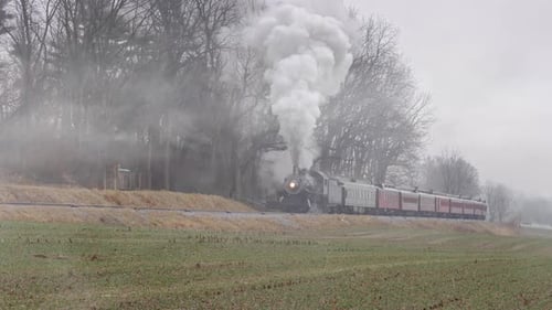 A Steam Engine and Passenger Cars Traveling Up Grade in a Lite Snow, Rain Mix