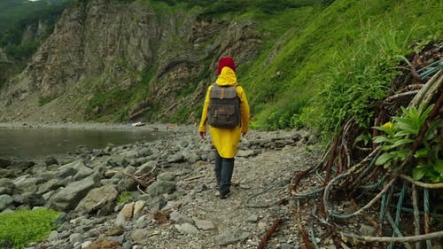 Person Walks on Rocky Beach in Yellow Raincoat