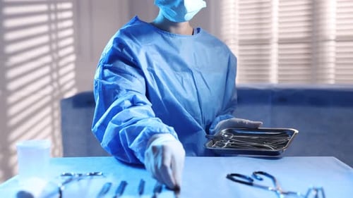 Doctor with different surgical tools at table in hospital, closeup