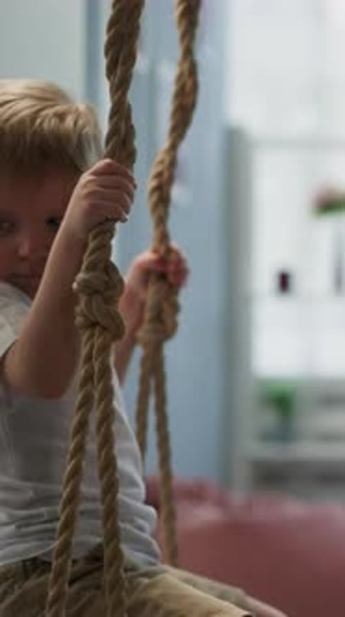 Calm Toddler Boy Rides on Swing in Light Living Room