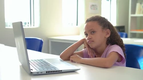 African girl child in purple shirt sitting at school facing laptop, camera moving, appearing bored