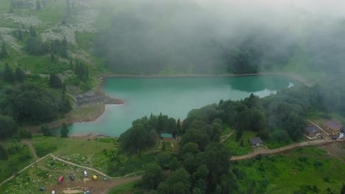 Fog entering mountain valley creating mystical scenery around lake