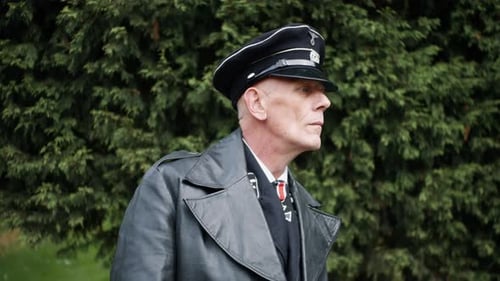 A world war two german nazi ss officer in a black uniform and leather jacket observing prisoners in