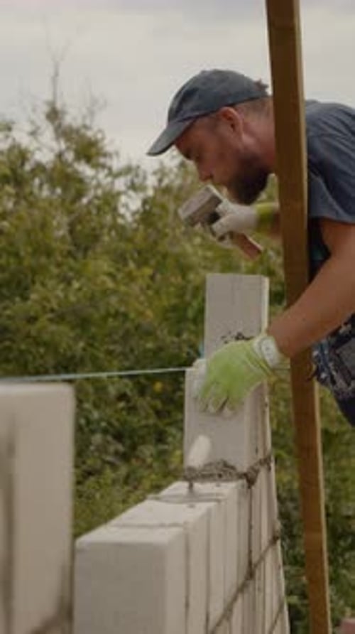 Vertical video Skilled worker builds a concrete brick wall for new home construction