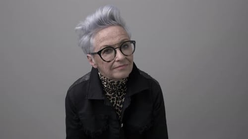 Stylish senior woman with gray hair and eyeglasses posing in studio setting
