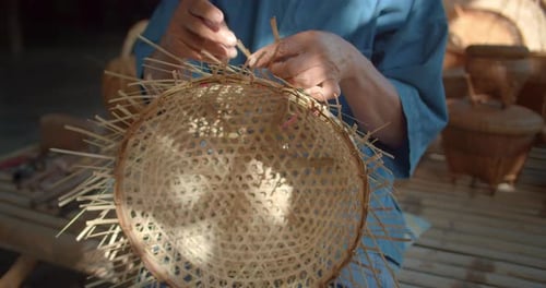 An Asian male farmer who is an elderly native basketry artisan weave basket from bamboo