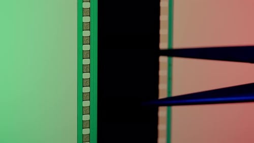 Scissors Cuts a Strip of Photographic Film on a Green and Pink Background Close Up