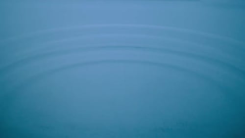 Macro Shot of a Drop of Water Falls on a Blue Liquid Surface Creating Water Rings and Waves