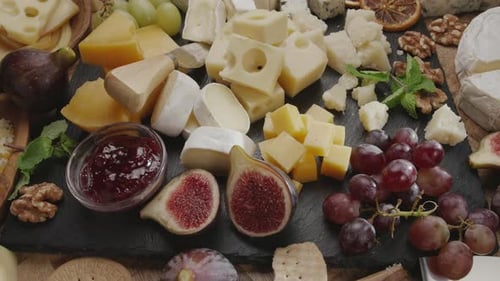 Variedade de queijos fatiados com frutas, hortelã, nozes e facas de corte de queijo.