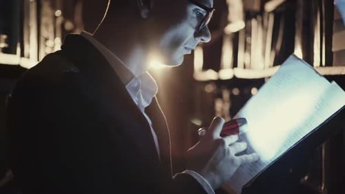 Ein junger Mann mit Taschenlampe schaut nachts in Bibliotheken nach Dokumenten