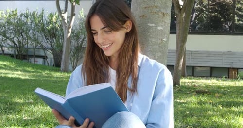 Young Smiling Woman Reading a Book in a Park Under a Tree
