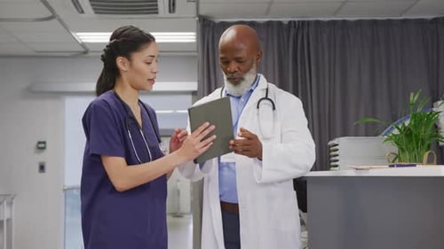 Diverse male and female doctors using tablet and talking at hospital