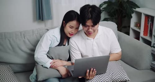 Happy Couple Using Laptop on Gray Couch Indoors