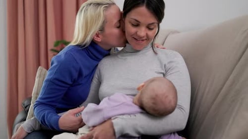 Authentic gay lesbian couple of mothers and newborn baby having tender moment at home - Lgbt family