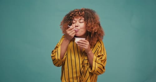 Woman Enjoying Yogurt Snack Against Blue Background