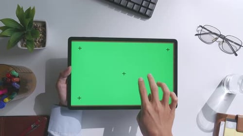 Top down view of man's hands using a mock up green screen tablet on white desk