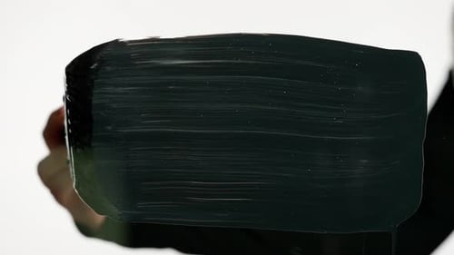 Femme utilisant un pinceau à l'huile acrylique, peinture noire moyenne et dessinant un trait large directement sur le verre
