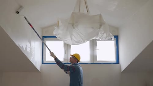 Ein Mann malt eine Wand mit einer Rolle und repariert das Zimmer im Dachgeschoss