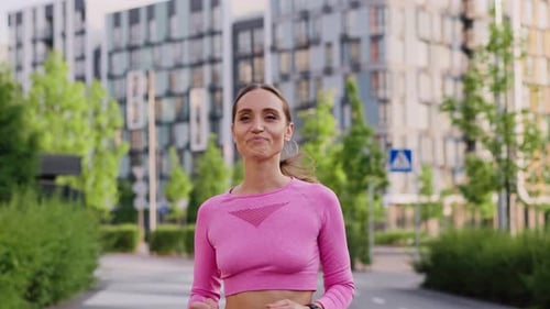 A Young Sportive Girl Jogger Outdoors in the City Park Among Modern Residential Highrise Buildings A