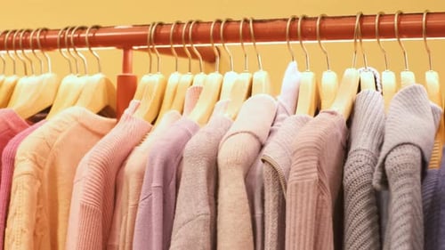 Warm pink knit sweaters hang on hangers in the store close-up.