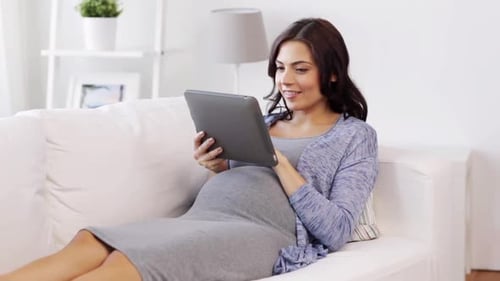 беременная женщина счастливо смотрит на результаты расчета в планшете