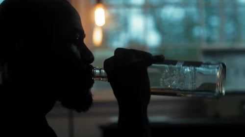 Man sits in dark room drinking alcohol