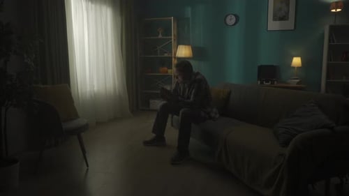 Smartphone Addiction and Depression Sad Young Man Sitting in a Dark Room on the Couch with a Phone