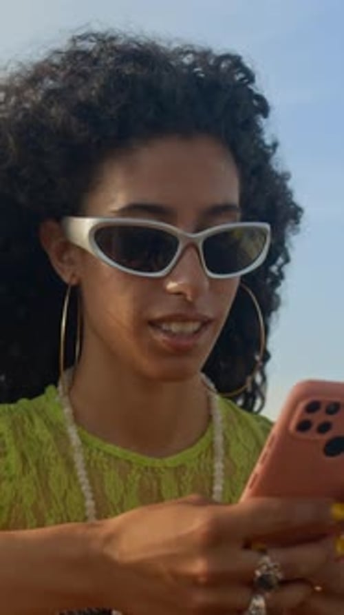 Stylish young woman using phone outdoors in bright light