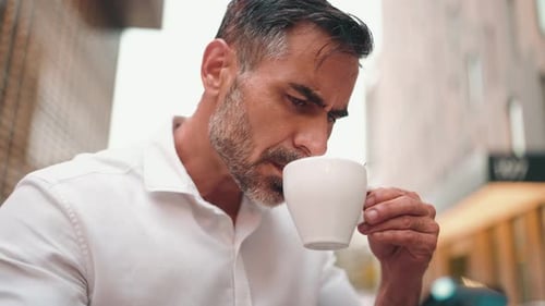 Mature businessman sitting at cafe table, drinking coffee and typing on smartphone