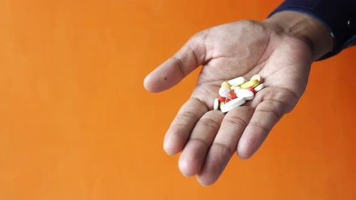 Hand eines Mannes mit Medizin aus dem Pillenbehälter verschüttet