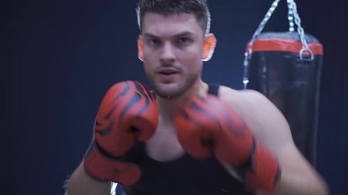 Aggressive male boxer professionally boxing in a dark gym.