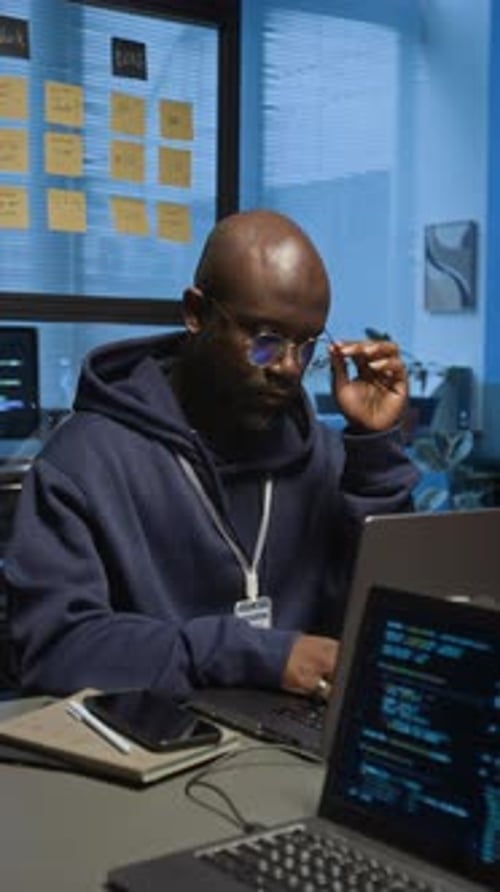 Man Working on Multiple Laptops in Dark Office