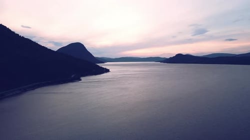 Flying aerial over the quiet ocean in Norway with the sky tinted by the sunrise sun