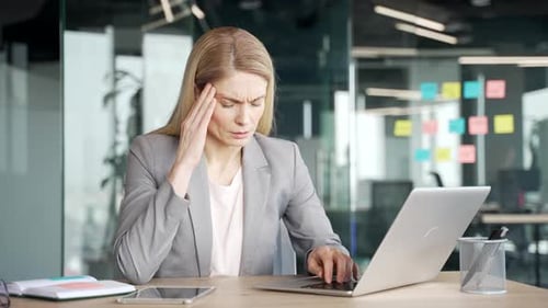 Stressed Woman Massaging Temples While Working at Laptop