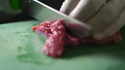 chef in a white gloves in the restaurant kitchen. Preparing food. The cook cuts the raw meat with a