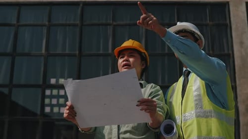 Architect and engineer work together on floor plan drawings outside construction site building