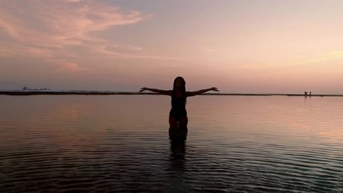 Silhouette einer Frau, die ihre Hände oder offene Arme hebt, wenn die Sonne aufgeht. Eine junge, schlanke, achtsame Frau
