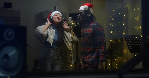 Portrait of Two Multiethnic Professional Singers in a Recording Studio, Wearing Santa Hats, Singing