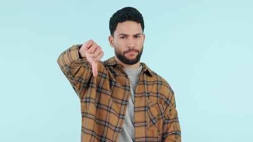 Thumbs down, negative review or feedback with a man in studio on a blue background to reject