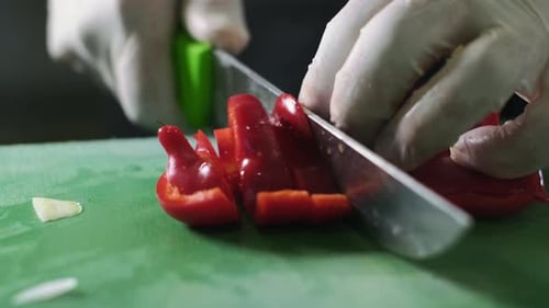 Close up man's hand slicing red fresh pepper on a cutting board with sharp knife. Chef is cutting re