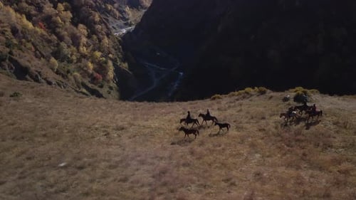 Drone over people on horseback walking along a precipice on a mountain