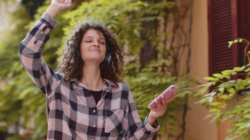 Happy Young Woman in Wireless Headphones Choosing Listening Music Dancing Outdoors City Street