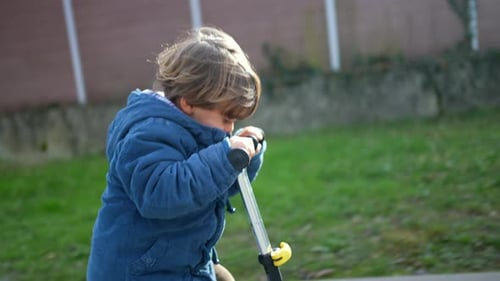 Child riding three wheeled schooter ouside in motion. One active 3 year old little boy rides toy