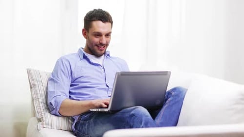 Cheerful Man Relaxing at Home Typing on Laptop