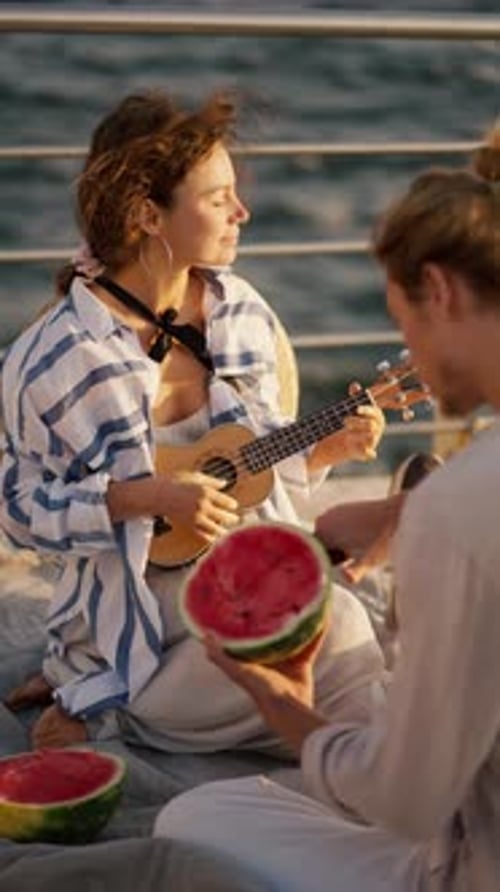 Vertical Video of a Happy Couple on a Date On the Pier Near the Sea the Guy Cuts a Watermelon the