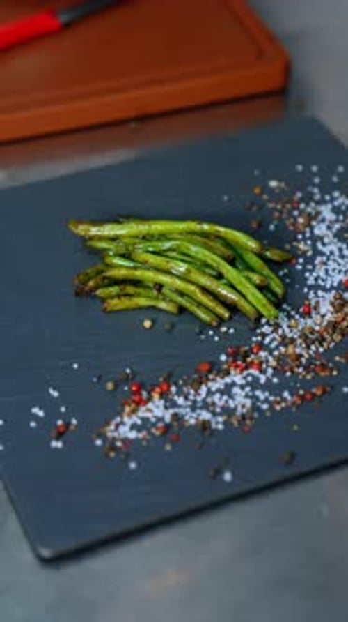 Fried green beans are put on the black charcuterie board. The plate is decorated with salt and peppe