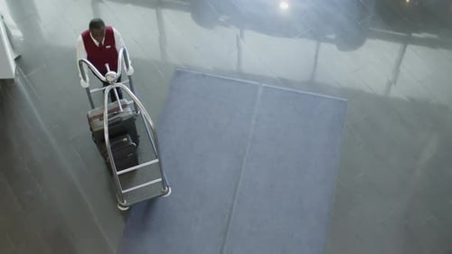 Portero de arriba hacia abajo del hotel arrastrando el carro de equipaje por el lobby