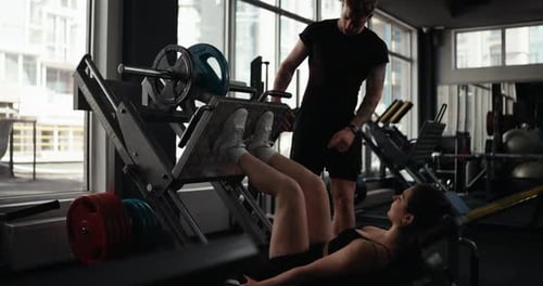 Woman Doing Leg Press with Trainer in Gym